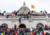 Crowd at U.S. Capitol building with flags and cameras.