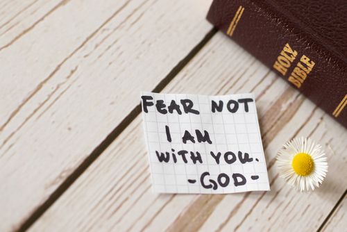 Note with Bible and daisy on wooden table.