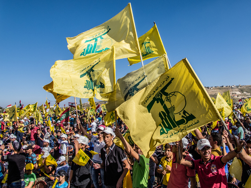 People waving Hezbollah flags at a large outdoor gathering.