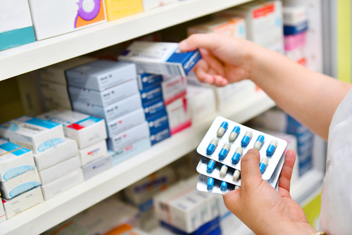 Person selecting medication from pharmacy shelf.